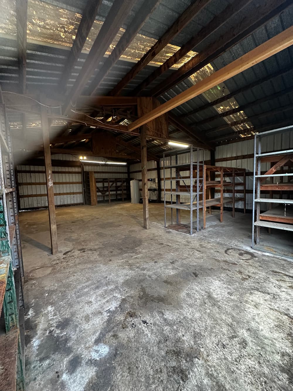 Spacious, empty warehouse interior with wooden beams and metal shelves.