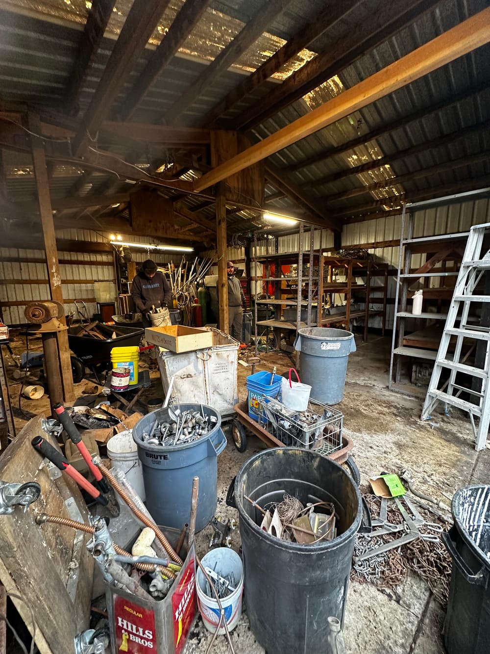 Cluttered workshop interior with various tools, buckets, and equipment scattered throughout.